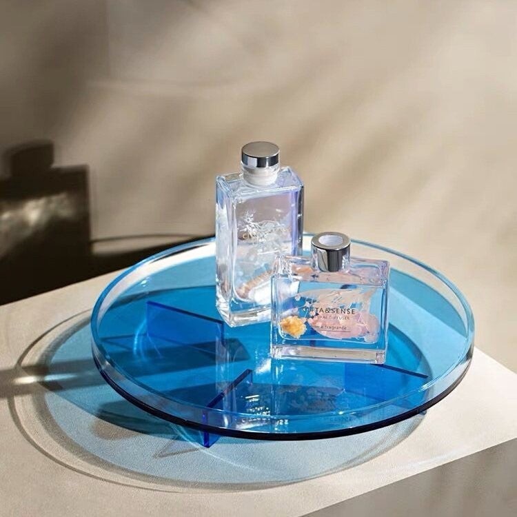 Cosik Home blue transparent acrylic round display tray with geometric raised base holding two glass bottles.