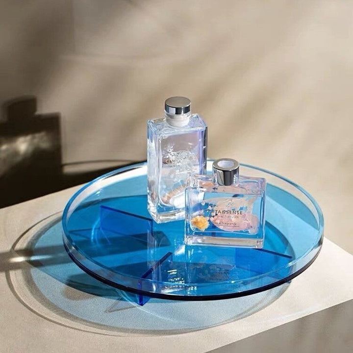 Cosik Home blue transparent acrylic round display tray with geometric raised base holding two glass bottles.