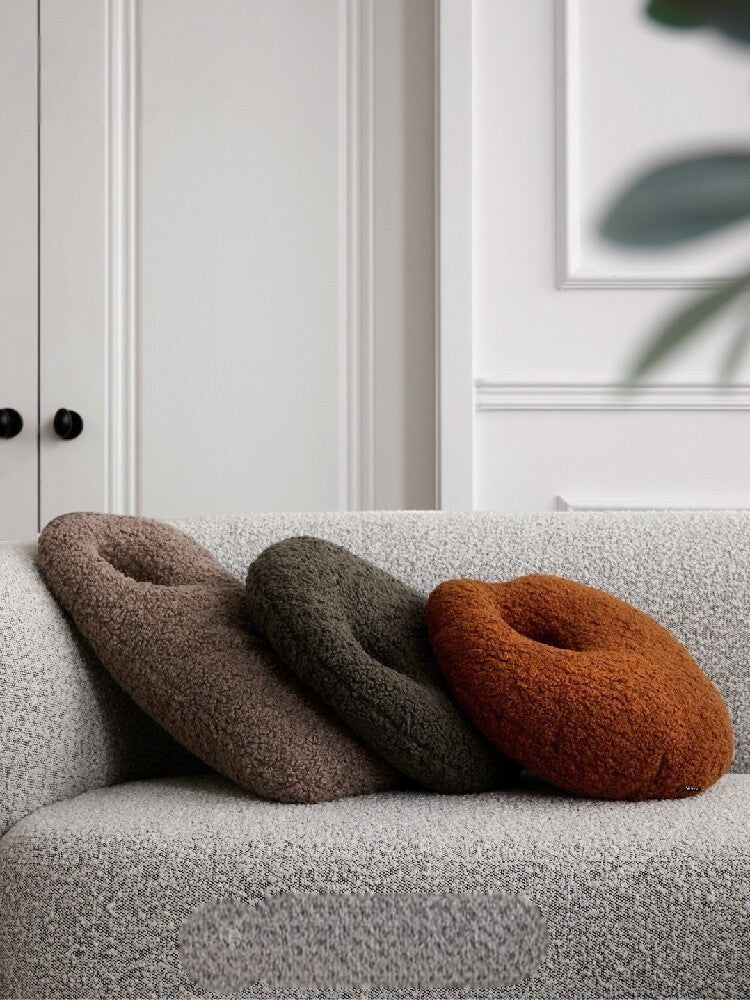 Cosik Home Abstract Bouclé Donut Throw Pillow in rust, olive green, and taupe on a textured grey sofa.