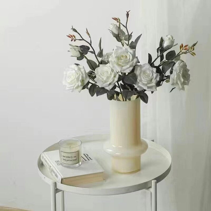 Cosik Home cream glass vase with white roses and greenery, on a side table with a book and candle.