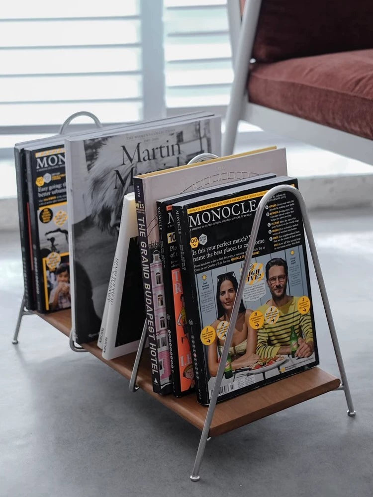 Cosik Home modern metal and wood magazine rack holding various magazines and books. Features a minimalist silver metal frame and a warm brown wood shelf.