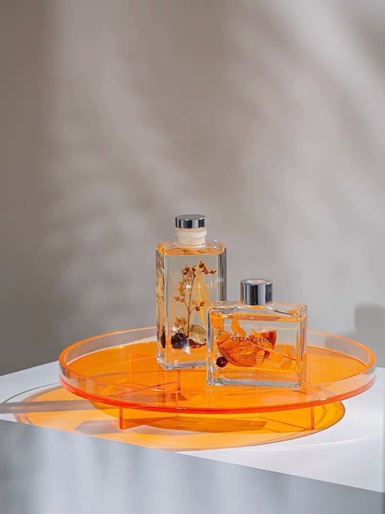 Cosik Home orange acrylic circular display tray with raised geometric base, holding two glass bottles.