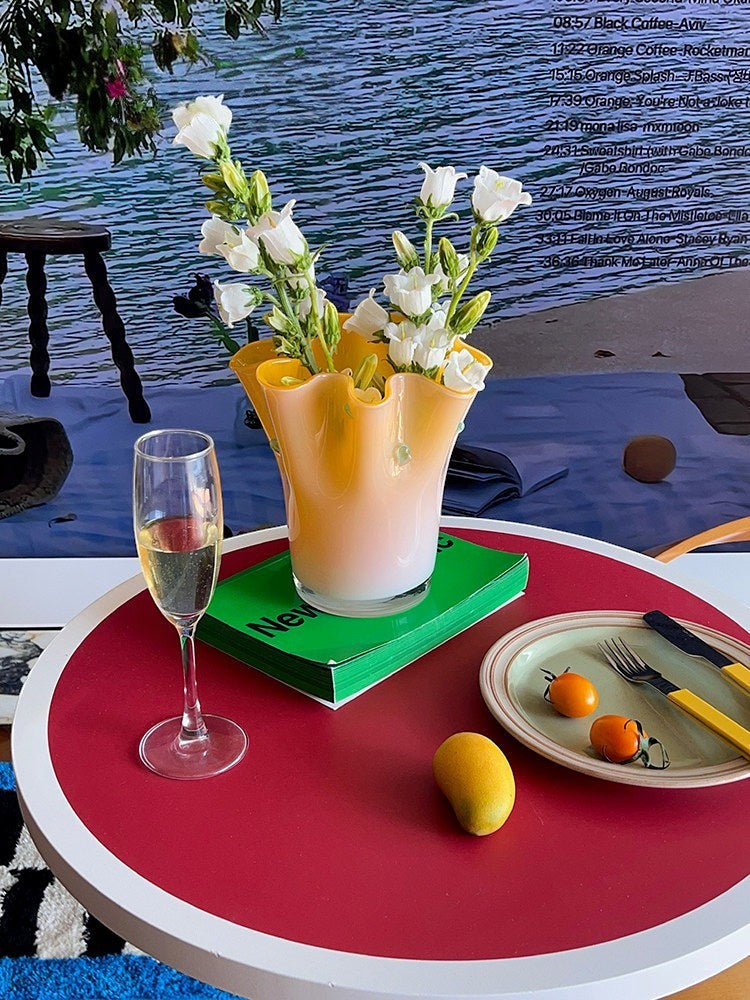 Cosik Home large orange glass vase with white flowers, on a green book, on a red table.