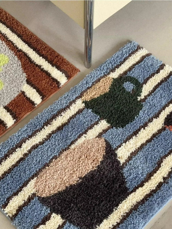 Cosik Home retro tufted plush bath mat with blue, cream, brown, and black stripes and a green kettle graphic.