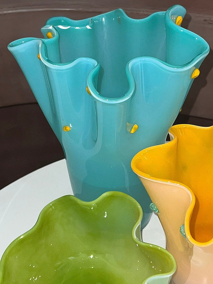 Cosik Home handmade turquoise glass vase with ruffled edges and yellow accents, next to green and orange vases.