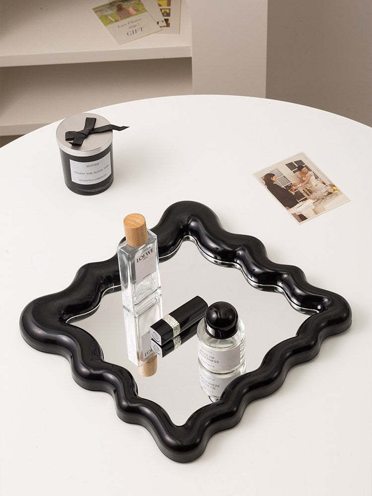 Cosik Home black wavy mirror vanity tray displaying perfumes and lipstick. Sculptural decor.